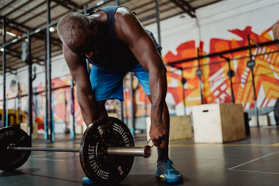 An African American man lifting a barbell in a vibrant gym with graffiti walls.