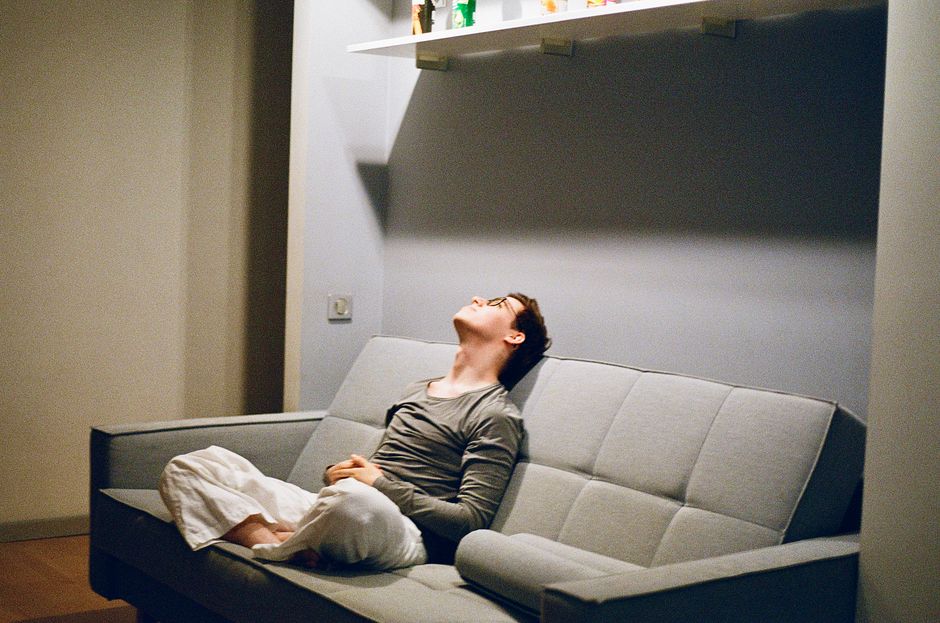 Man in casual attire sitting relaxed on a sofa, looking up indoors, in a cozy room.