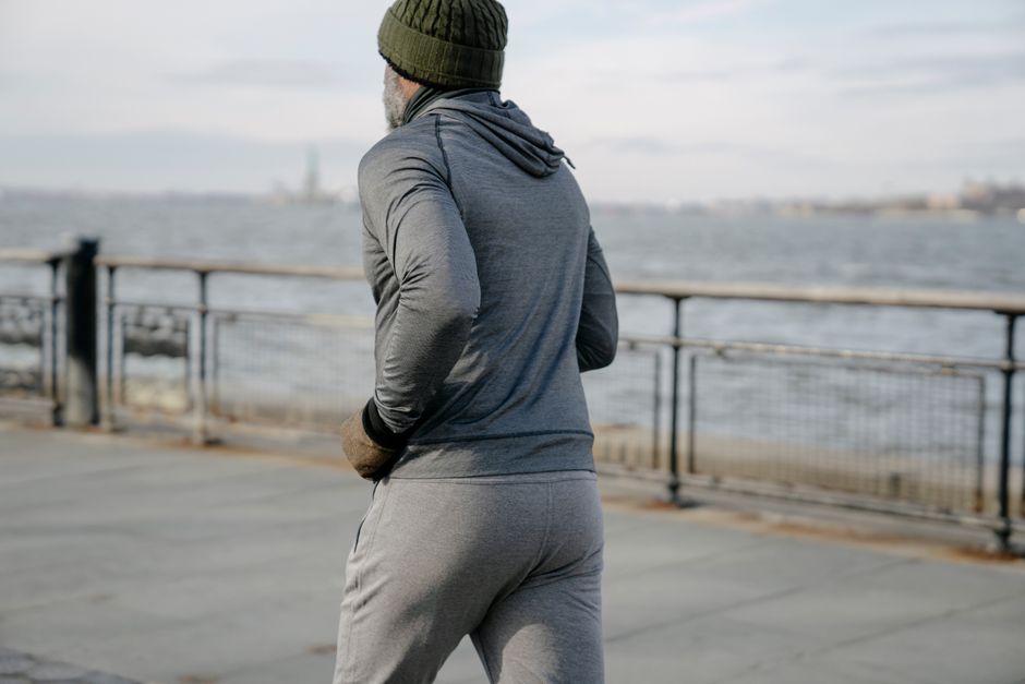 Back view of anonymous bearded African American male runner running on embankment near water during training at morning time