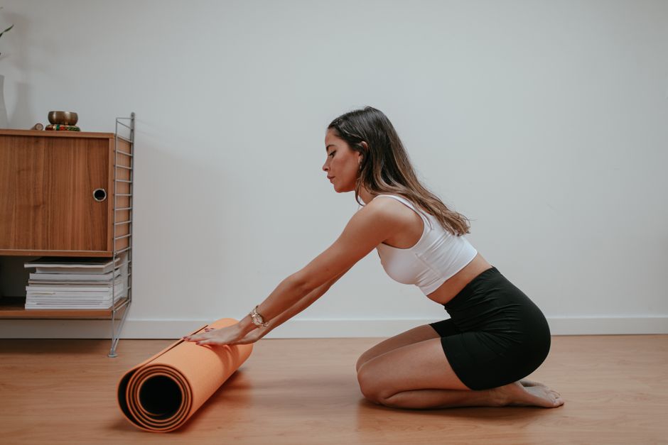 Woman in activewear rolling an orange yoga mat in a modern home setting.