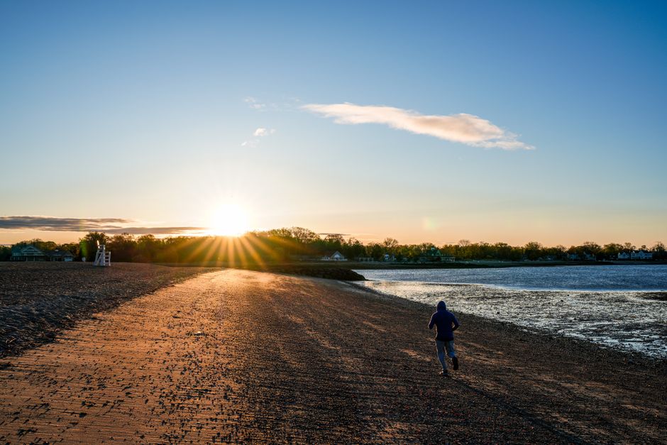 A lone runner jogs along the beach at sunrise in Cove Island Park, Stamford, Connecticut.