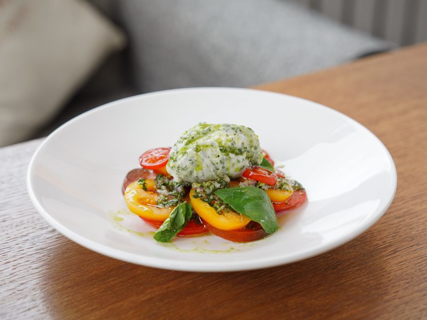 A vibrant Caprese salad featuring cherry tomatoes and pesto ricotta on a white plate indoors.