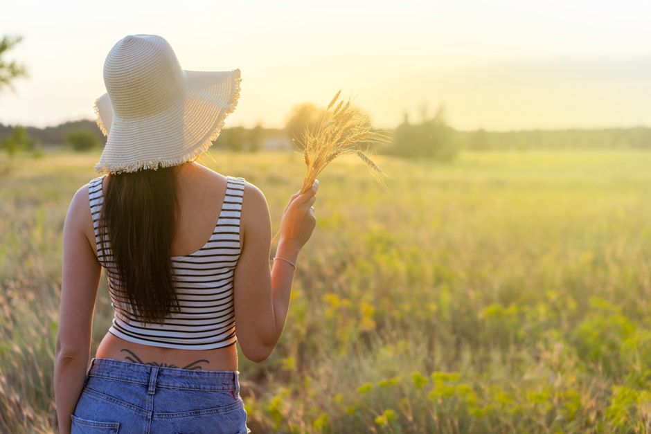 Young woman with straw hat in sunlit field at sunset, embracing relaxation and nature.