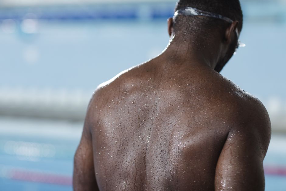 Close-up of a shirtless man with water droplets on his back, at an indoor pool.