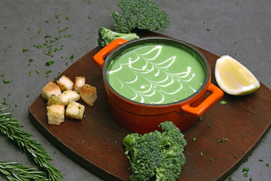Creamy broccoli soup in an orange pot paired with croutons and lemon for a healthy meal.